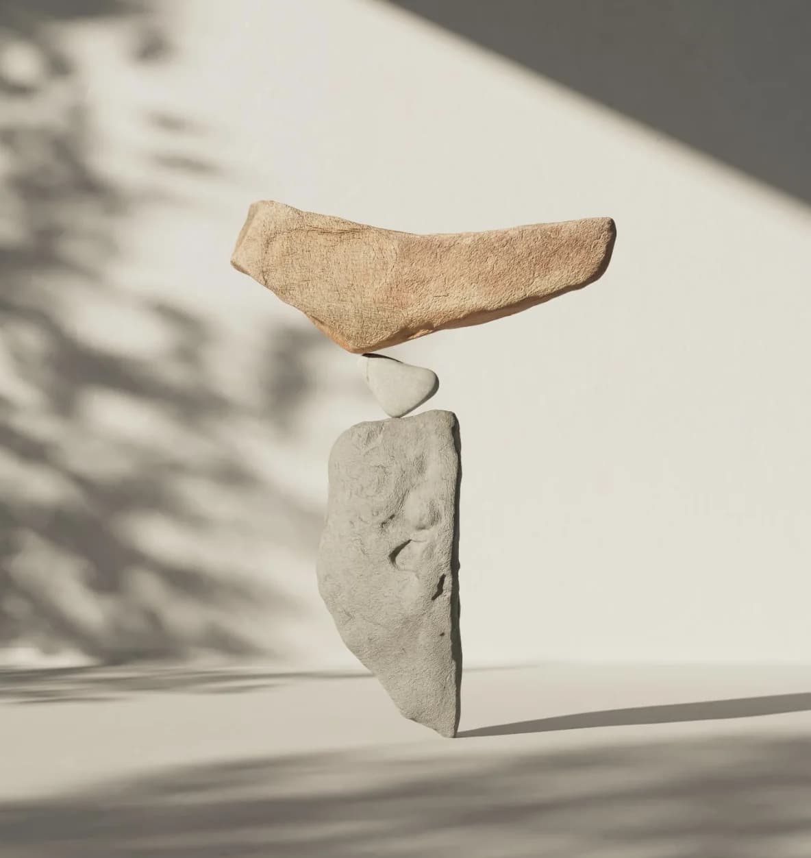 Three stones balanced one on another against a pale wall, leaf shadows falling across them