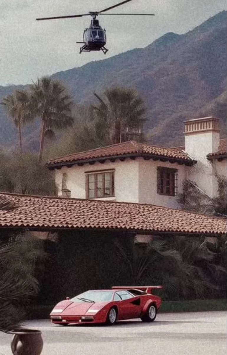 A helicopter comes in low over a Spanish-style villa with terracotta roofs and palms, a red wedge-shaped sports car waiting in the drive below the mountains